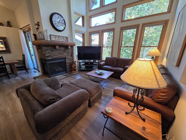 A living room with a fireplace, a television, leather sofas, a coffee table, and a lamp. - Snowcreek Resort Vacation Rental 848 (Mammoth Lakes)