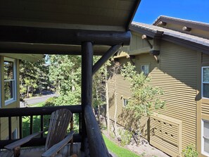 A wooden deck with a chair, a house with a sloped roof, and a clear sky.