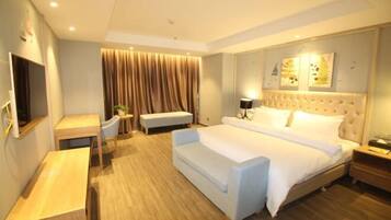 A hotel room with a large bed, a desk, a bench, and a TV.
