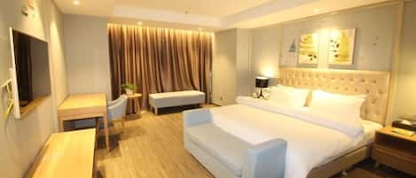 A hotel room with a large bed, a desk, a bench, and a TV.