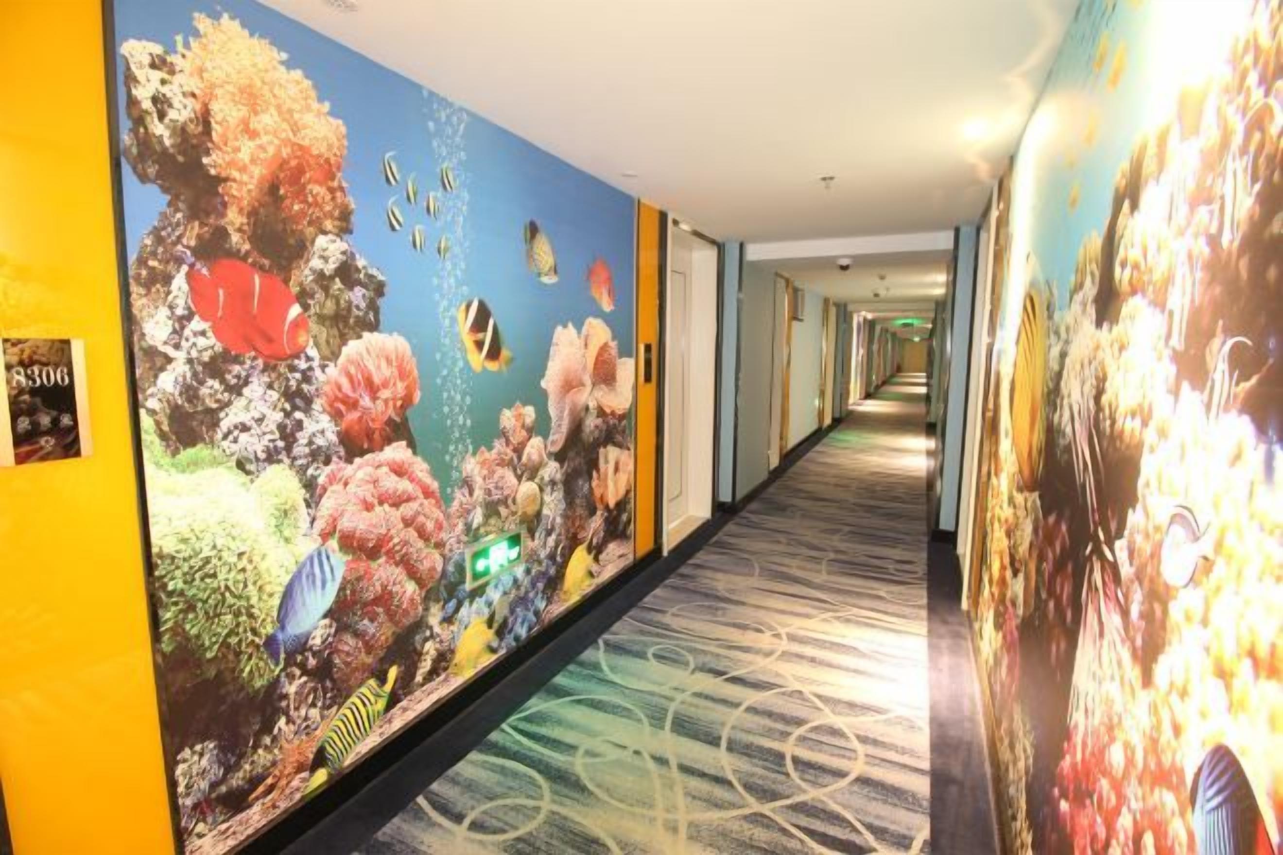 A hotel corridor with a long hallway, a carpeted floor, and walls adorned with large, colorful murals.