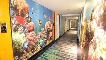 A hotel corridor with a long hallway, a carpeted floor, and walls adorned with large, colorful murals.
