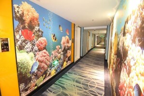 A hotel corridor with a long hallway, a carpeted floor, and walls adorned with large, colorful murals.