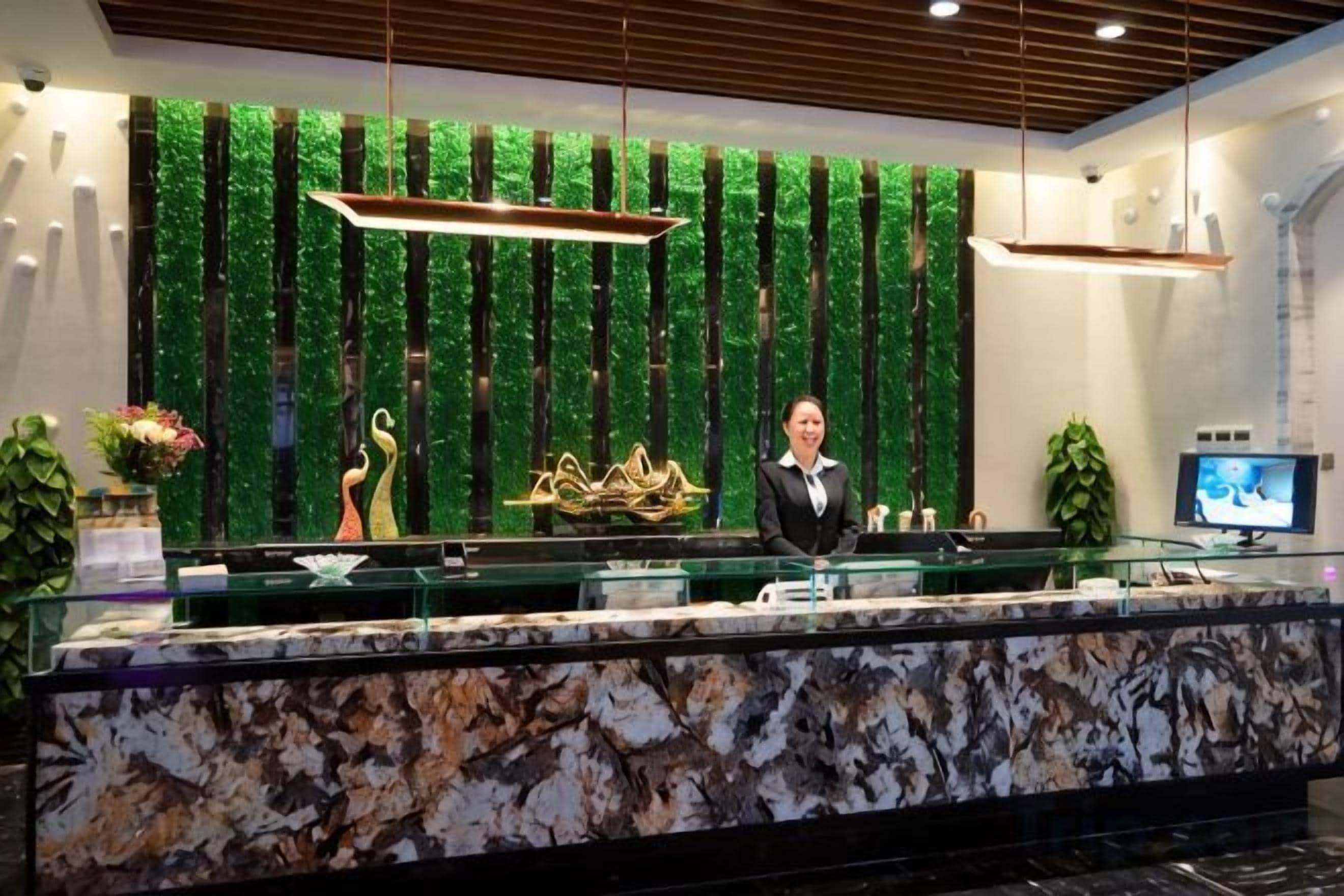 A reception desk with a marble top, a green vertical plant wall, and a television screen.