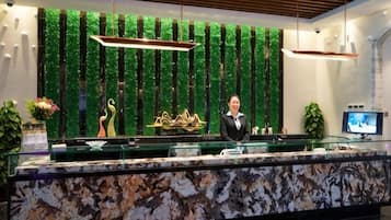 A reception desk with a marble top, a green vertical plant wall, and a television screen.