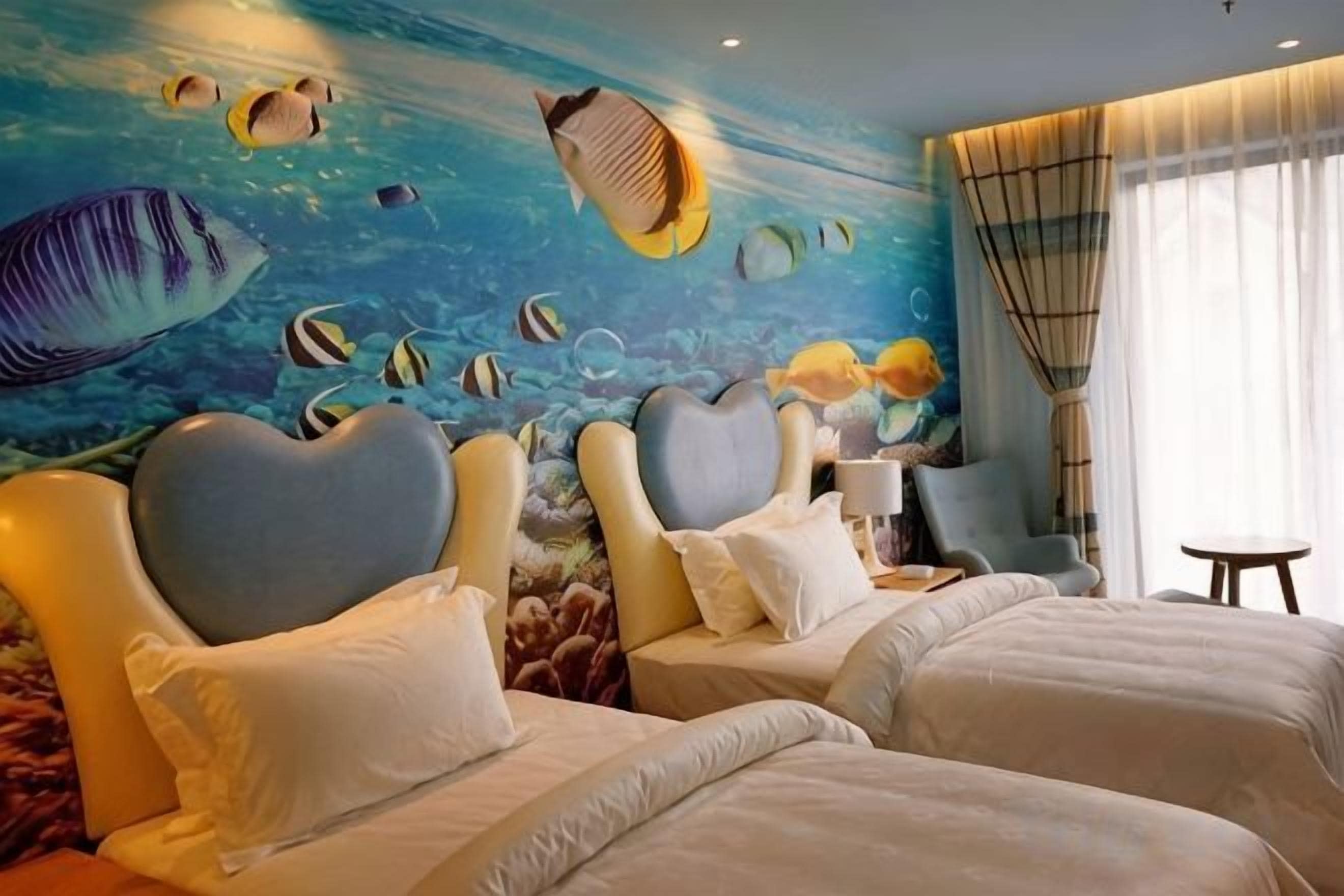 A hotel room with two beds, a mural of an underwater scene, and a view of the ocean through the window.