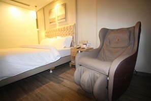 Une chambre d’hôtel équipée d’un lit, d’un fauteuil massant, d’une table de chevet avec un téléphone et une bouteille d’eau.