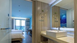 Habitación de hotel moderna con un ventanal grande, tocador de madera con lavabo y cama con vista a la ciudad.