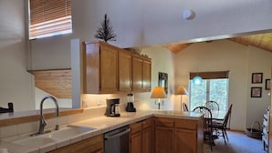 A kitchen with wooden cabinets, a dishwasher, a coffee maker, and a dining area with a table and chairs. - Snowcreek Resort Vacation Rental 644 (Mammoth Lakes)