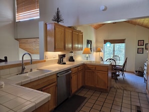 A kitchen with wooden cabinets, a dishwasher, a coffee maker, and a dining area with a table and chairs.
