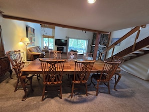 A dining area with a wooden table and chairs, a sofa, a TV, and a staircase.