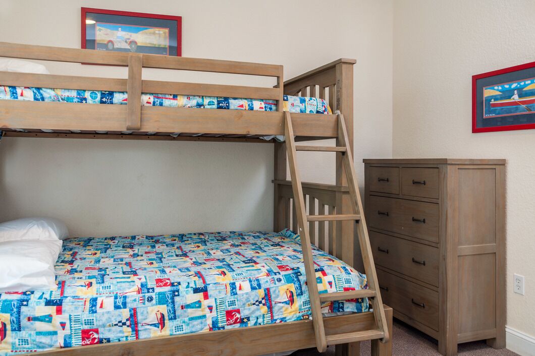 A bunk bed with a colorful quilt, a wooden ladder, and a dresser with multiple drawers.