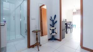 Een moderne badkamer met een glazen douchecabine, een houten deur en een klein, rond tafeltje met een fles.