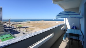Een balkon met een tafel en stoelen, met uitzicht op een strand en een parkeerplaats.