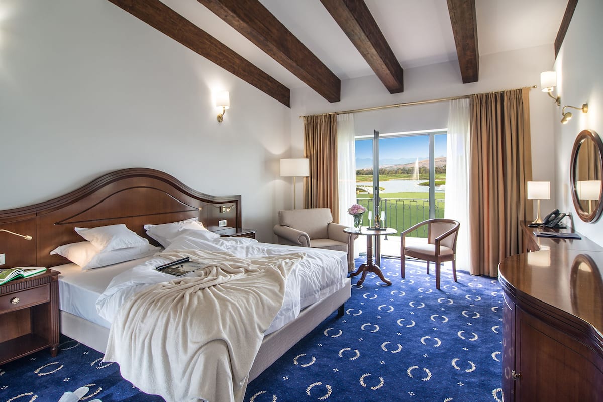 Habitación de hotel con una cama grande, un escritorio, una silla y vistas a un campo de golf.