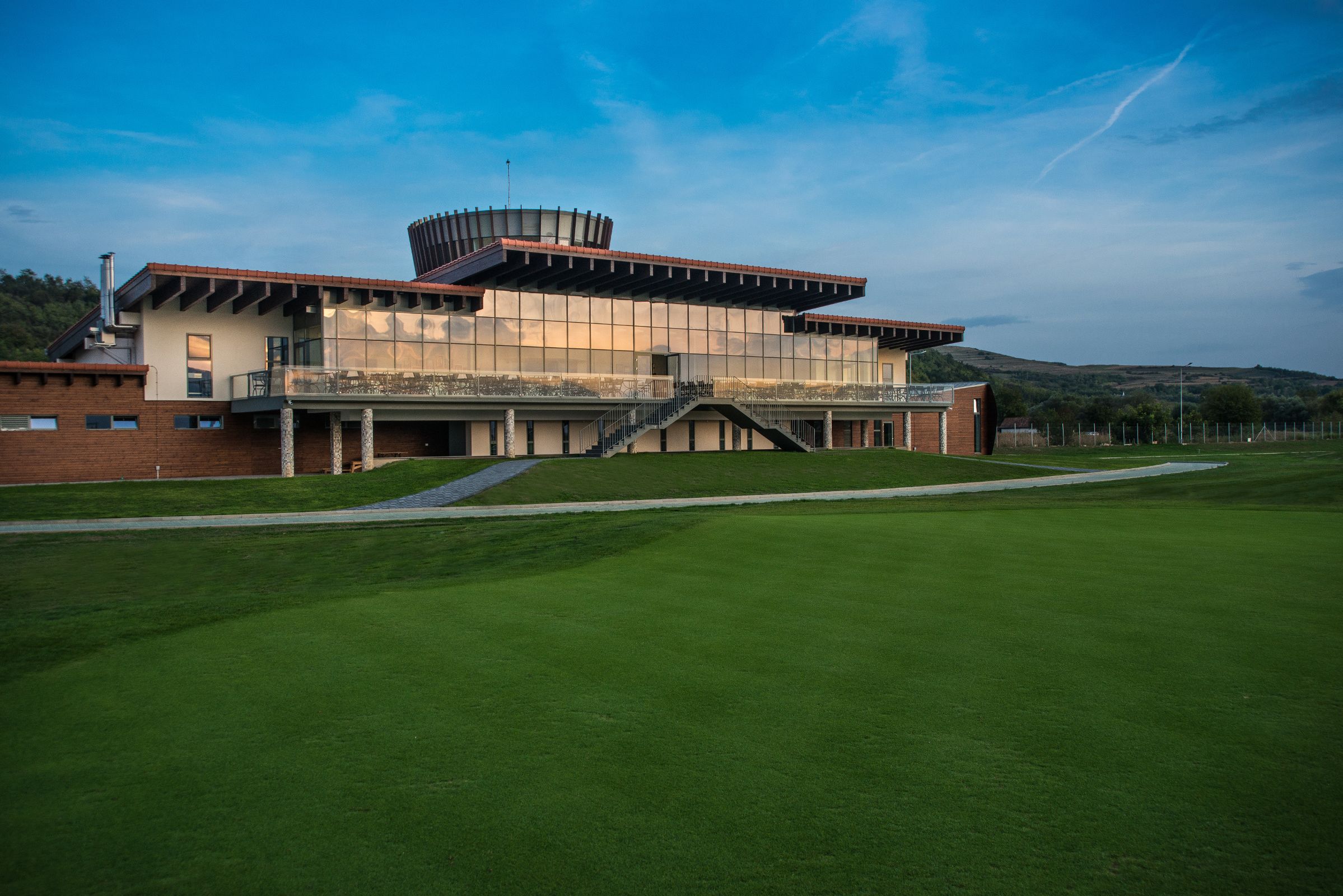 A modern building with a flat roof, large windows, and a staircase leading to a balcony.