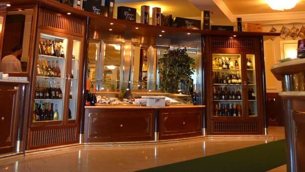A bar area with a hexagonal stained glass ceiling, wooden bar counters, and shelves with bottles. - Giada Hotel Ristorante (Grumolo delle Abbadesse)