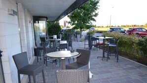 An outdoor patio with wicker chairs and tables, a parking lot in the background, and a building with a tiled facade. - Giada Hotel Ristorante (Grumolo delle Abbadesse)