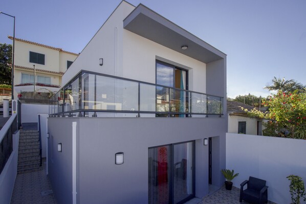 A modern two-story house with a balcony, large windows, and a staircase leading to the upper floor.