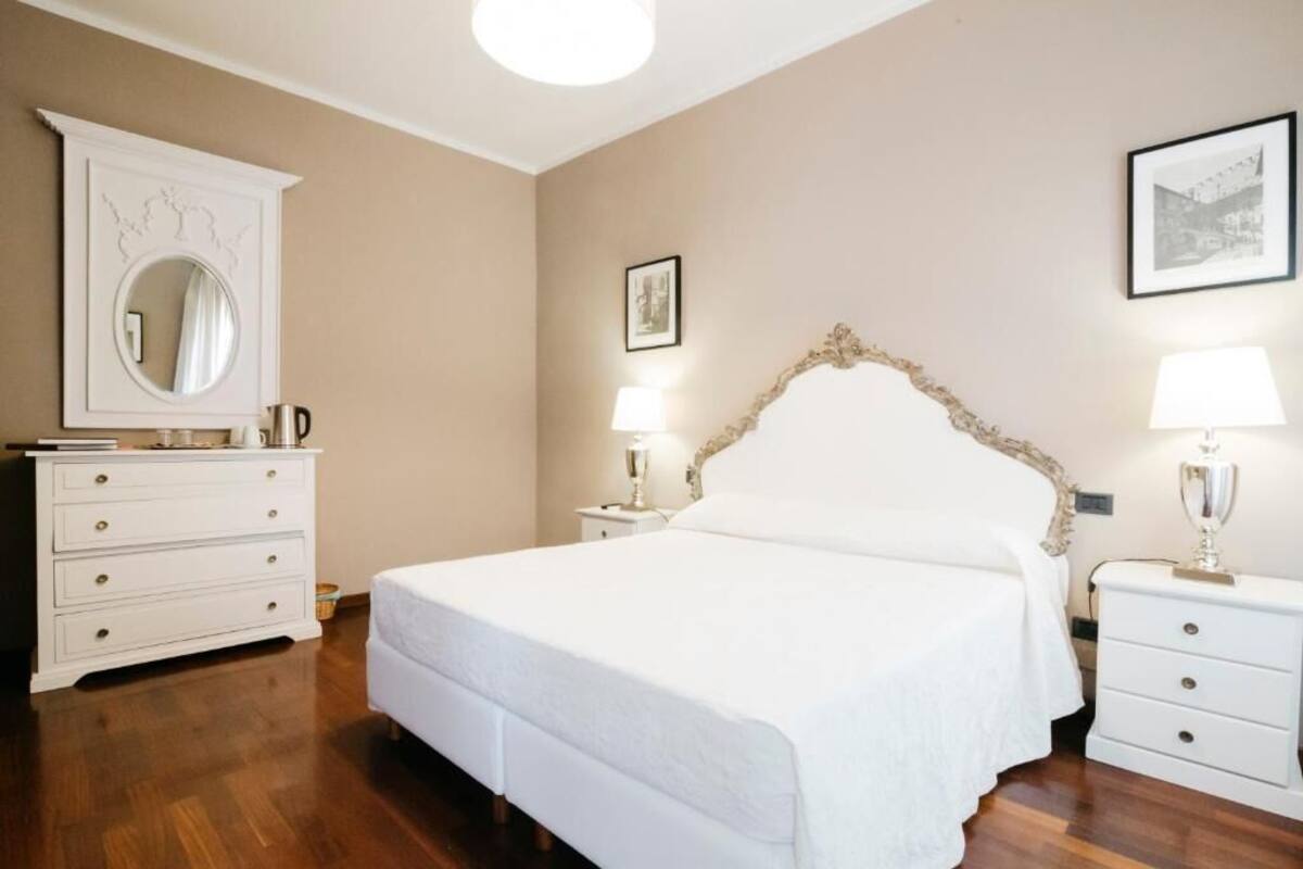 A bedroom with a large bed, white nightstands, a dresser, a mirror, and framed pictures on the walls.
