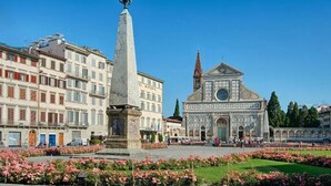 A square with a tall monument, a church with a dome, and surrounding buildings. - Residenza Ognissanti  (Florence)
