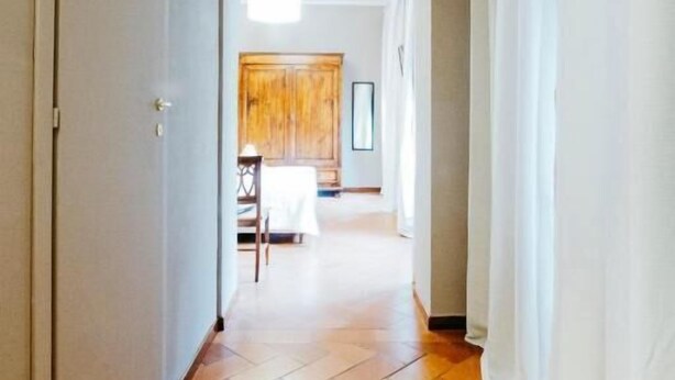 A hallway with a tiled floor leading to a room with a wooden cabinet and a table. - Residenza Ognissanti  (Florence)