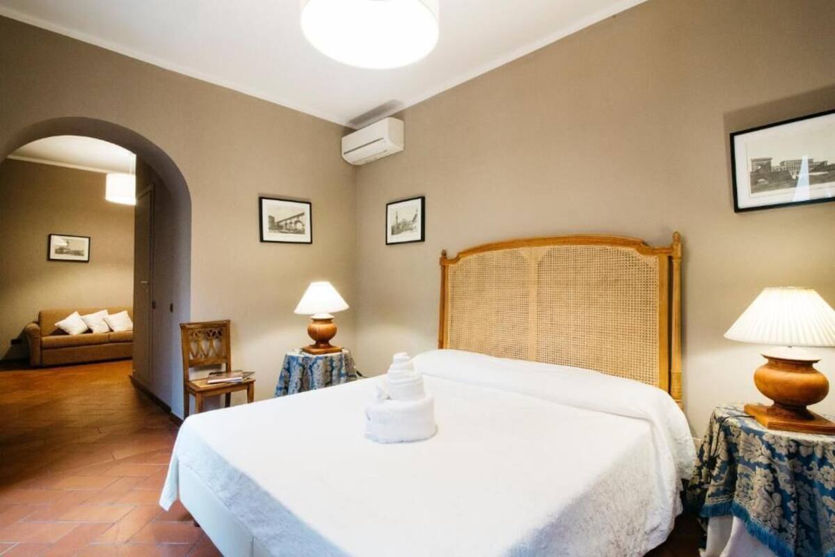 A hotel room with a bed, a chair, a table with a lamp, and a wall-mounted air conditioner.