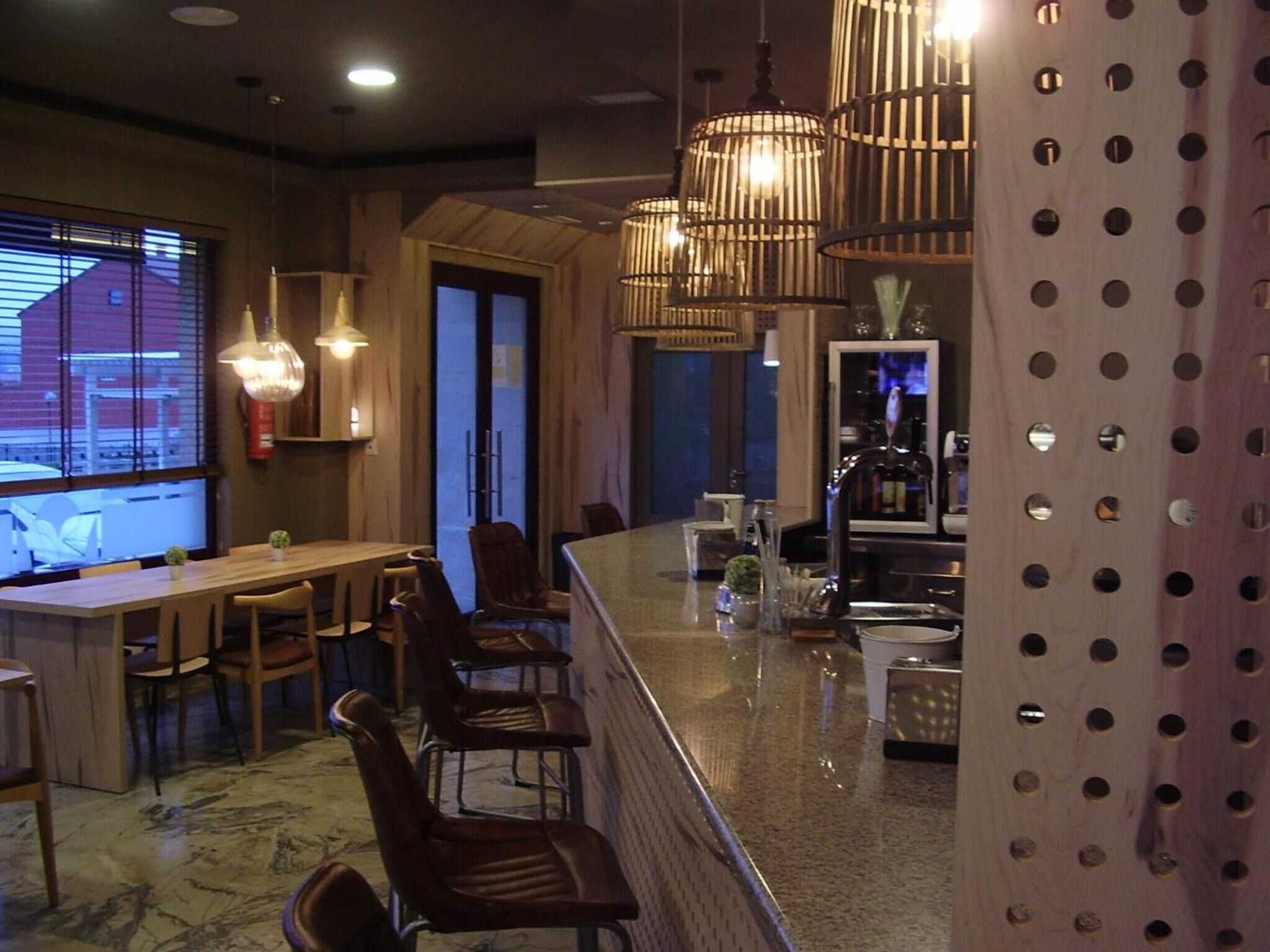 A restaurant interior with a bar area, wooden furniture, and hanging pendant lights.