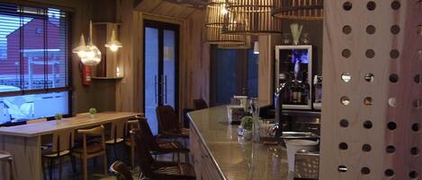 A restaurant interior with a bar area, wooden furniture, and hanging pendant lights.