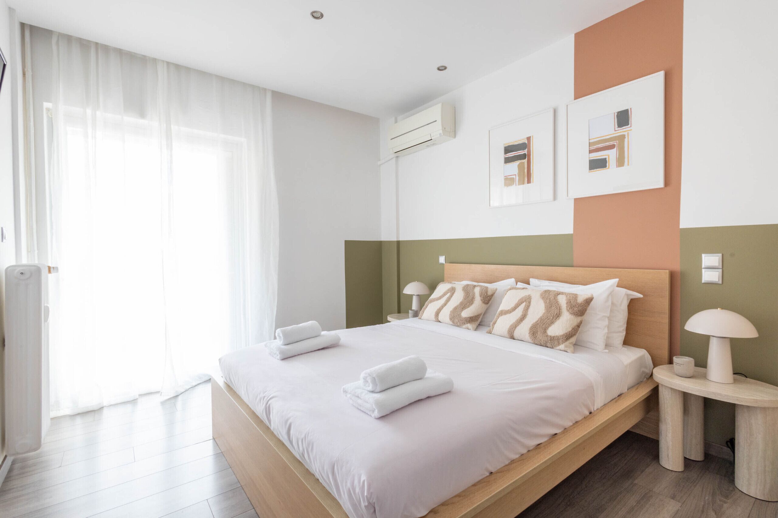 Ein modernes Hotelzimmer mit einem hölzernen Bett, weißen Laken, einer Nachttischlampe und einem Kunstwerk an der Wand.