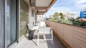 A balcony with a table and chairs, a sliding door, and a view of buildings and trees.