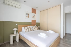 Una cama bien tendida con sábanas y toallas blancas, una mesita de noche con lámpara y un aire acondicionado de pared.