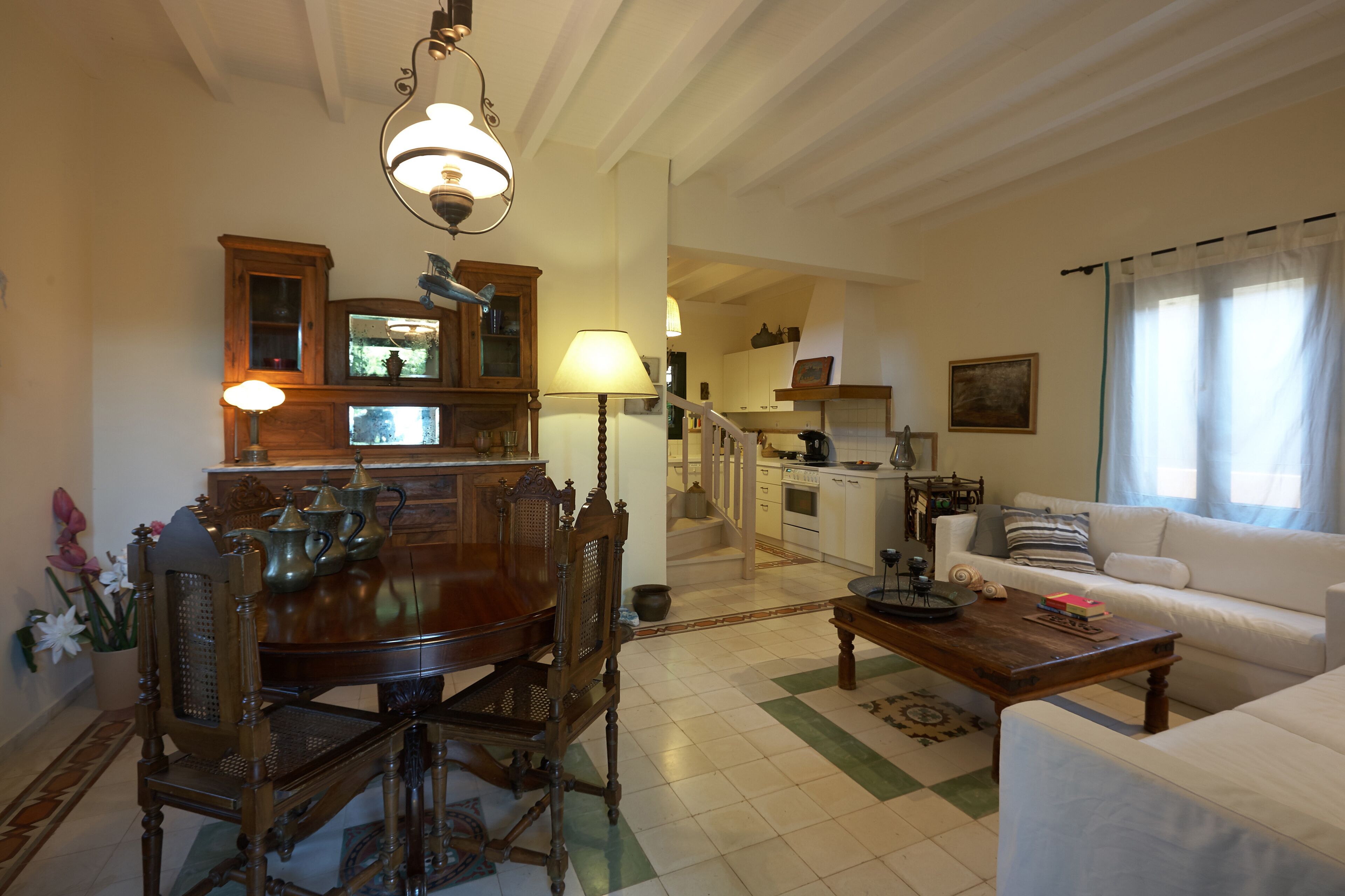 A spacious living room with a dining area, a kitchen in the background, and a staircase leading to an upper floor.