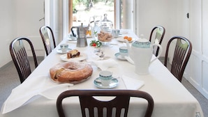 A dining area with a table set for six, featuring a large cake, teapot, and various dishes.