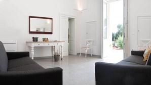 A modern living room with two dark sofas, a white console table with decorative items, a white chair, and a large window with a view of greenery.