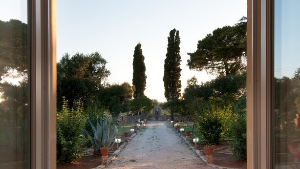 A view from a room through a glass door, leading to an outdoor garden with two chairs and a pathway.