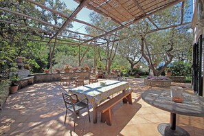 An outdoor patio with a table and chairs, surrounded by potted plants and trees.