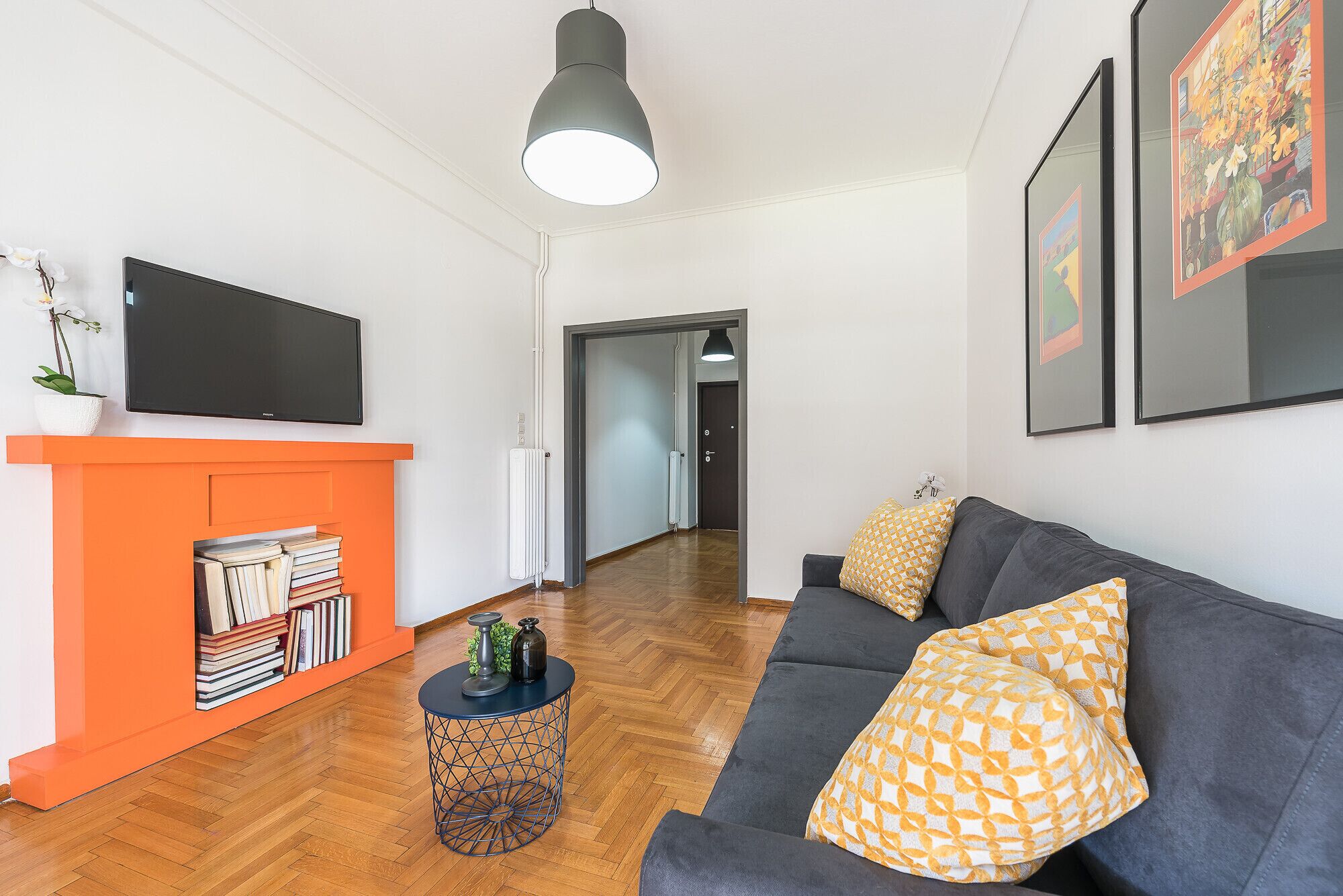 Un salon moderne avec un canapé gris, une cheminée orange et un téléviseur fixé au mur.