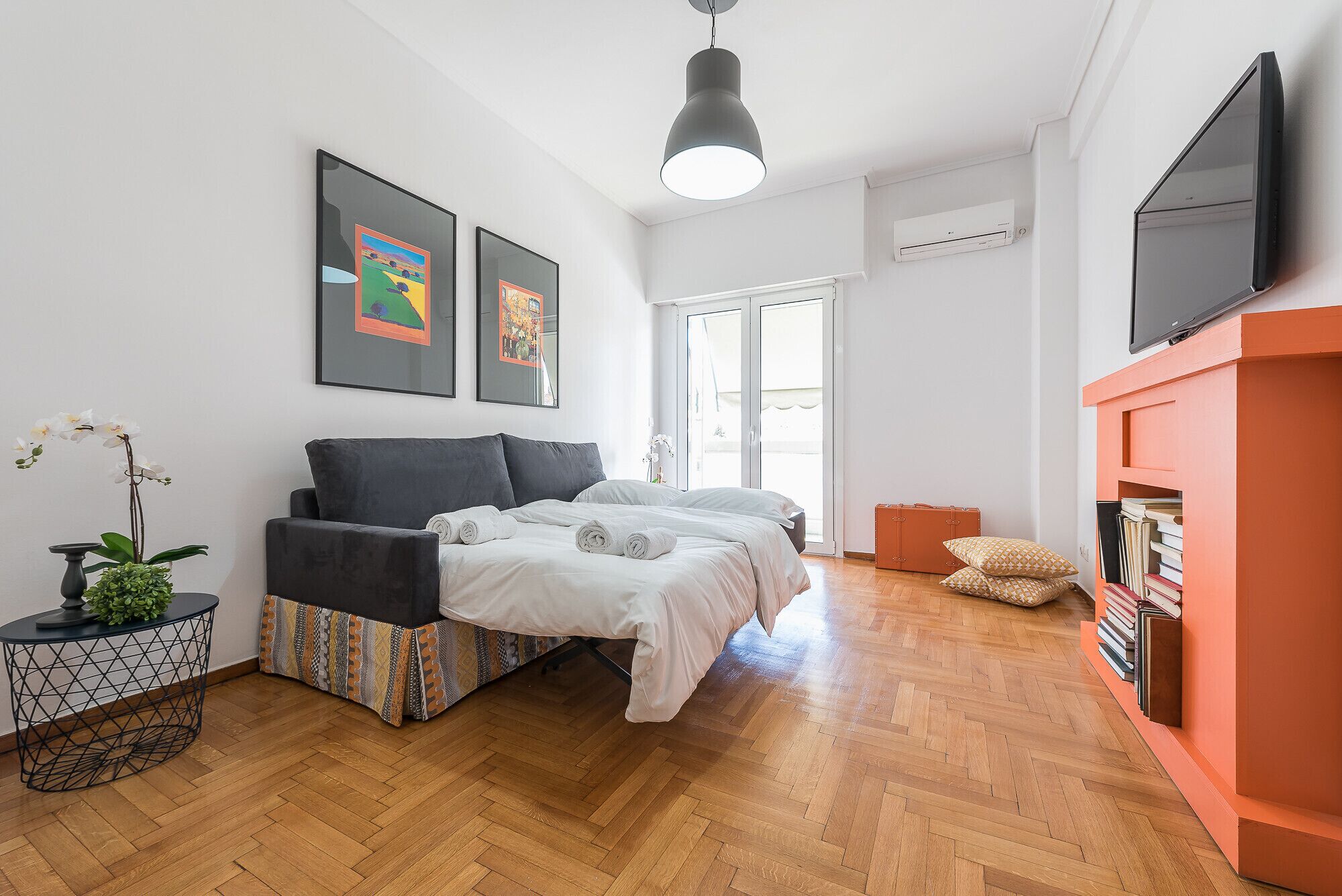 A modern bedroom with a bed, a small table with a plant, a TV, and a bookshelf.