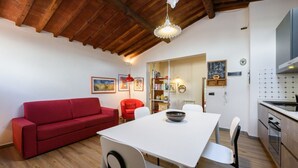 A dining area with a white table and chairs, a red sofa, and a kitchen with a stove and oven. - Apartment Cappelle Medicee Florence by Mmega (Firenze)