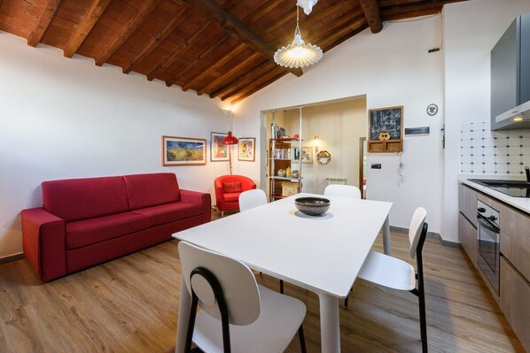 Un coin repas avec une table et des chaises blanches, un canapé rouge et une cuisine équipée d’une cuisinière et d’un four.