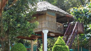 Una casa del árbol de madera con techo de paja, un balcón y una escalera.