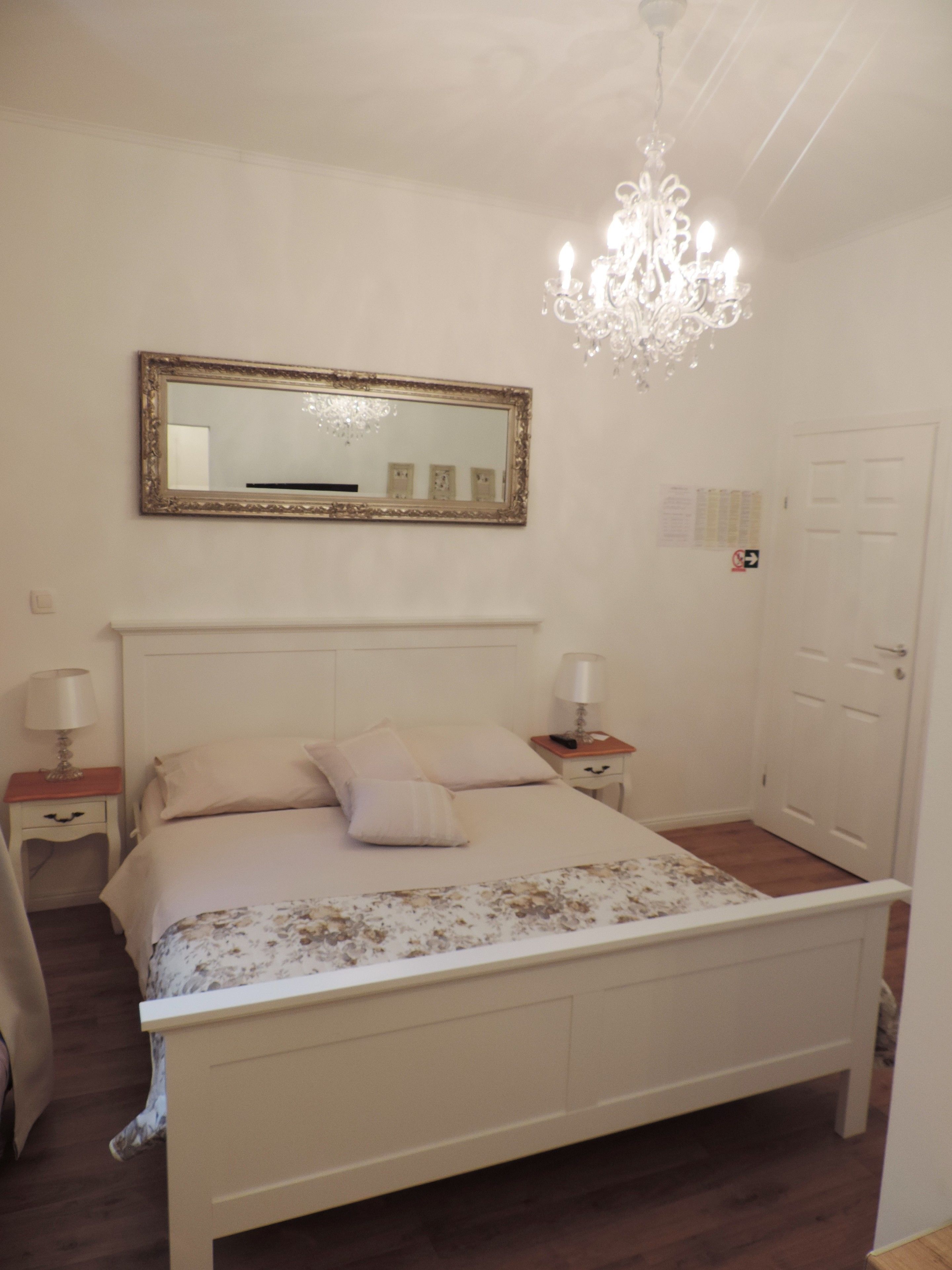 Une chambre à coucher avec un lit, un lustre, un miroir et une porte.