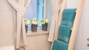 A bathroom with a window, a shelf with potted plants, a towel rack, and a shower. - Studios Ani (Split)