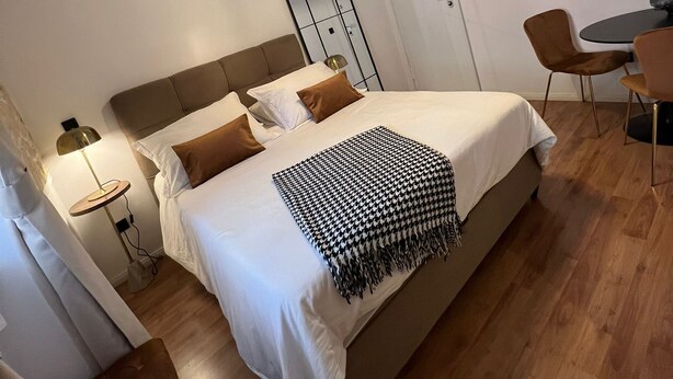 A modern hotel room with a large bed, a bedside table with a lamp, a small round table with chairs, and a ceiling light fixture. - Studios Ani (Split)