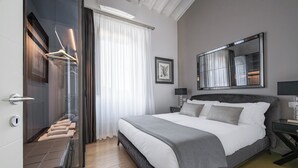 A modern hotel room with a large bed, a mirror, a wardrobe, and a bathroom with a glass door.