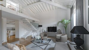 A spacious living area with a modern design, featuring a staircase, a glass coffee table, and a comfortable seating arrangement.