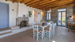 Un espace repas agrémenté d’une cheminée en pierre, de poutres apparentes en bois et d’une grande fenêtre.