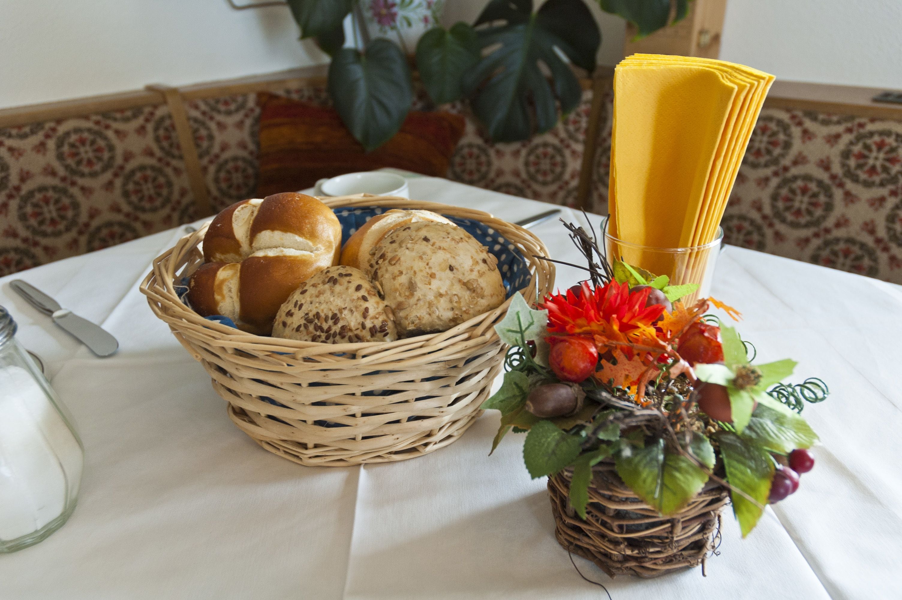 A table with a basket of bread, a small plant, and a folded yellow napkin.