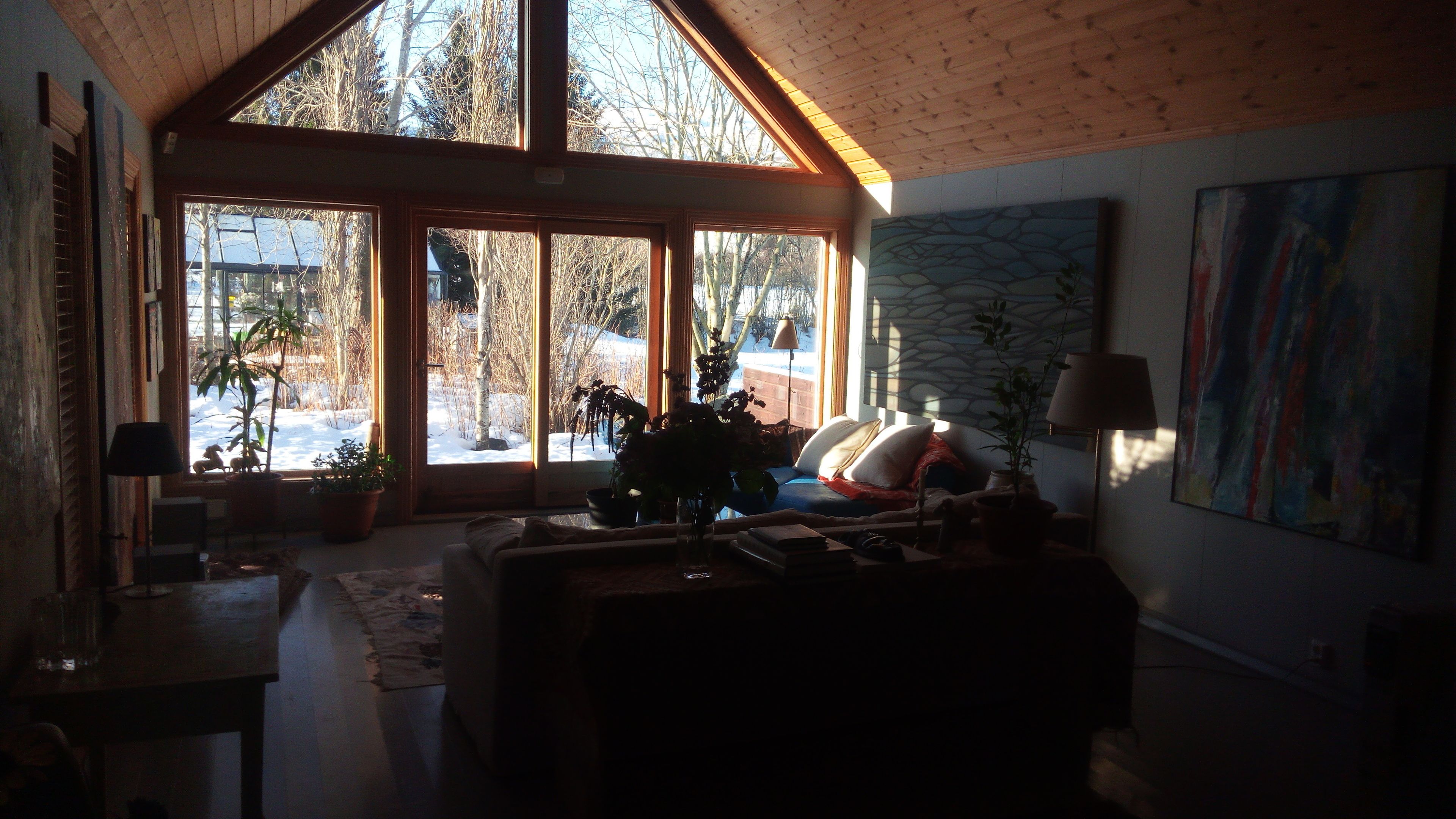 A cozy living room with a large window, a sofa, a coffee table, and a painting on the wall.